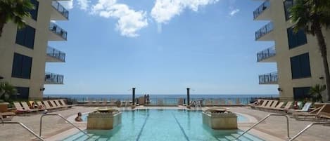 A pool area with clear water, lounge chairs, and a view of the ocean.
