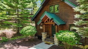 Une cabane en rondins, avec des fondations en pierre, un toit végétalisé et une véranda avec des marches menant à la porte.