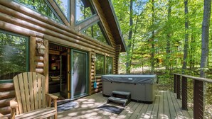 Une cabane en rondins avec une terrasse, un jacuzzi et une chaise.