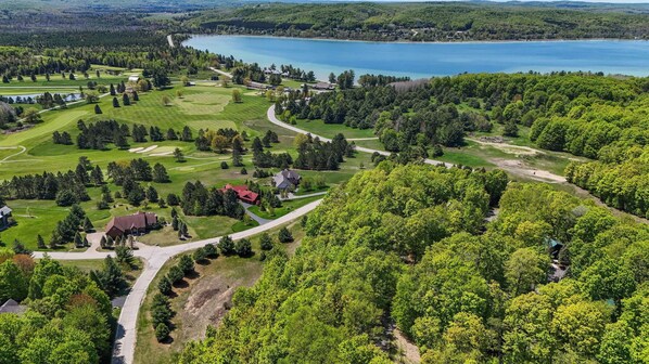 Vista aérea de um campo de golfe com um lago, rodeado por floresta densa e edifícios residenciais.