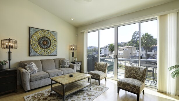 A spacious living room with a large window, a sofa, a coffee table, and two patterned armchairs.