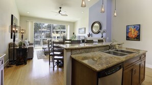 A modern kitchen with granite countertops, a dishwasher, and a dining area with chairs and a table.