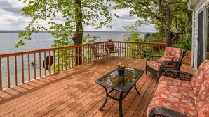 Une terrasse en bois offrant une vue sur un lac, aménagée avec des chaises et une table en osier, et dotée d’une rambarde sur le pourtour.