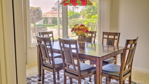 A dining area with a table and chairs, a vase with flowers, and a view of the outdoors.