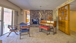 A living room with a stone fireplace, a piano, and a dining area with chairs and a table.