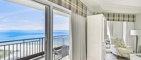 A balcony with a view of the ocean, a white wardrobe, and a patterned armchair.