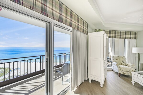 A balcony with a view of the ocean, a white wardrobe, and a patterned armchair.