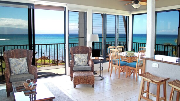A balcony with a view of the ocean, wicker furniture, a ceiling fan, and a bar area.