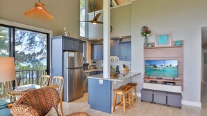 A modern kitchen with a large island, stainless steel appliances, and a TV mounted above the island.