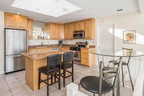Una cocina moderna con armarios de madera, electrodomésticos de acero inoxidable, una isla de vidrio y una mesa de comedor de vidrio.