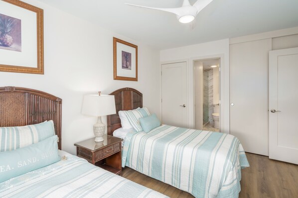 A hotel room with two beds, a nightstand, a lamp, and a ceiling fan.