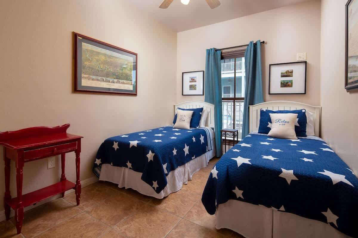 A room with two beds, a red table, and a window with curtains.