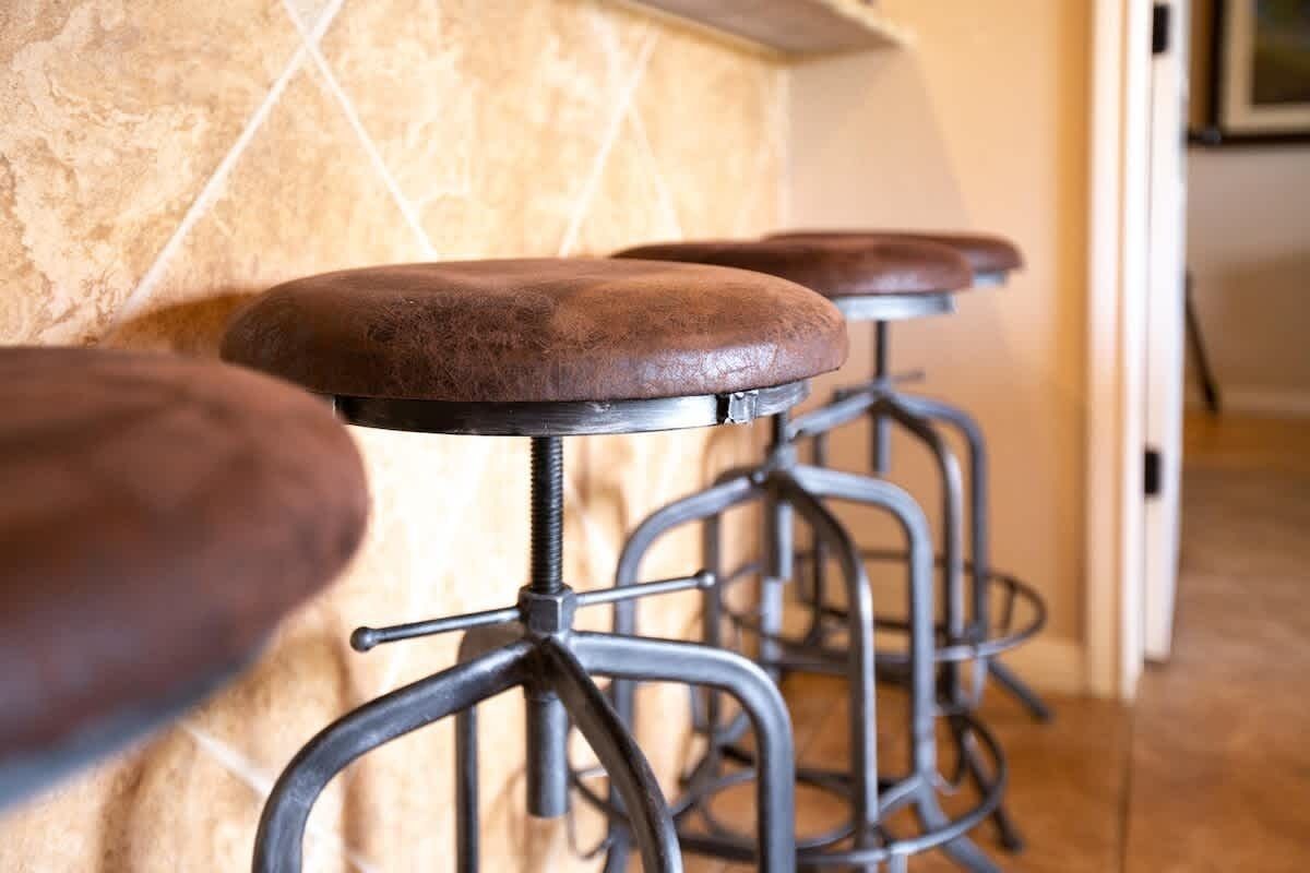 A row of bar stools with metal frames and cushioned seats, positioned against a wall with a tiled backsplash.