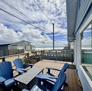 A wooden deck with blue Adirondack chairs and a table, overlooking a beach with a view of the ocean and a cloudy sky. - Dog Friendly Cottage with Ocean Views (Stinson Beach)