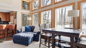 A kitchen with wooden cabinets, a black refrigerator, and a dining area with a table and chairs. - Newly Remodeled 780 Disciples Condo | Slopeside, short walk to Village Lane (Boyne Falls)