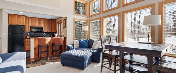 A kitchen with wooden cabinets, a black refrigerator, and a dining area with a table and chairs. - Newly Remodeled 780 Disciples Condo | Slopeside, short walk to Village Lane (Boyne Falls)