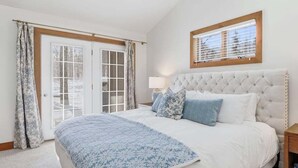 A bedroom with a large bed, a window with blinds, a bedside table with a lamp, and a wall-mounted TV. - Newly Remodeled 780 Disciples Condo | Slopeside, short walk to Village Lane (Boyne Falls)