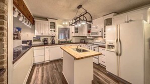 A kitchen with white cabinets, a wooden island, and a built-in microwave. - LD 1683 Texas River Haus (New Braunfels)