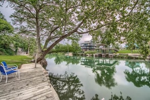 A wooden deck with blue chairs, a pond, and a building with a bridge.