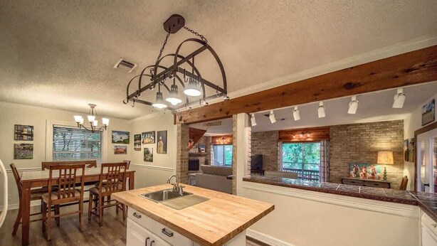 A kitchen with a wooden island, white cabinetry, and a hanging light fixture. - LD 1683 Texas River Haus (New Braunfels)
