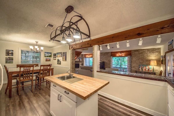 A kitchen with a wooden island, white cabinetry, and a hanging light fixture.