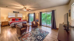 A bedroom with a bed, two chairs, a desk, a ceiling fan, and large windows with curtains. - LD 1683 Texas River Haus (New Braunfels)