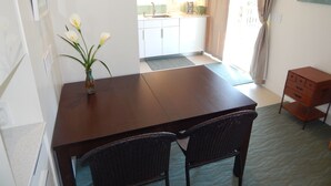 A dining area with a wooden table and two chairs, a vase with flowers, a kitchen in the background, and a small cabinet. - The Wright Spot.  A 1 bedroom with loft in the Heart of Wrightsville Beach! (Wrighsville Beach)