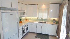 A modern kitchen with white cabinets, a stainless steel sink, a microwave, a kettle, and a coffee maker. - The Wright Spot.  A 1 bedroom with loft in the Heart of Wrightsville Beach! (Wrighsville Beach)