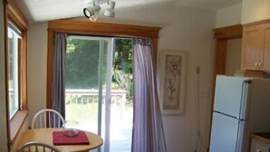 Una cocina pequeña con un refrigerador, una mesa de comedor con sillas y una puerta corrediza de vidrio que da a una terraza.