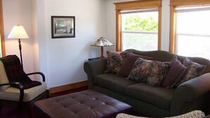 Una sala de estar con un sofá, un sillón, una lámpara y una ventana con vistas a zonas verdes.