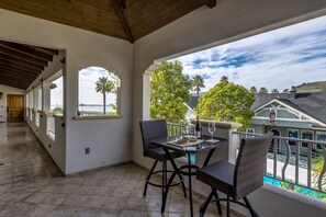 Een balkon met een tafel en stoelen, met uitzicht op een zwembad en palmbomen en huizen.