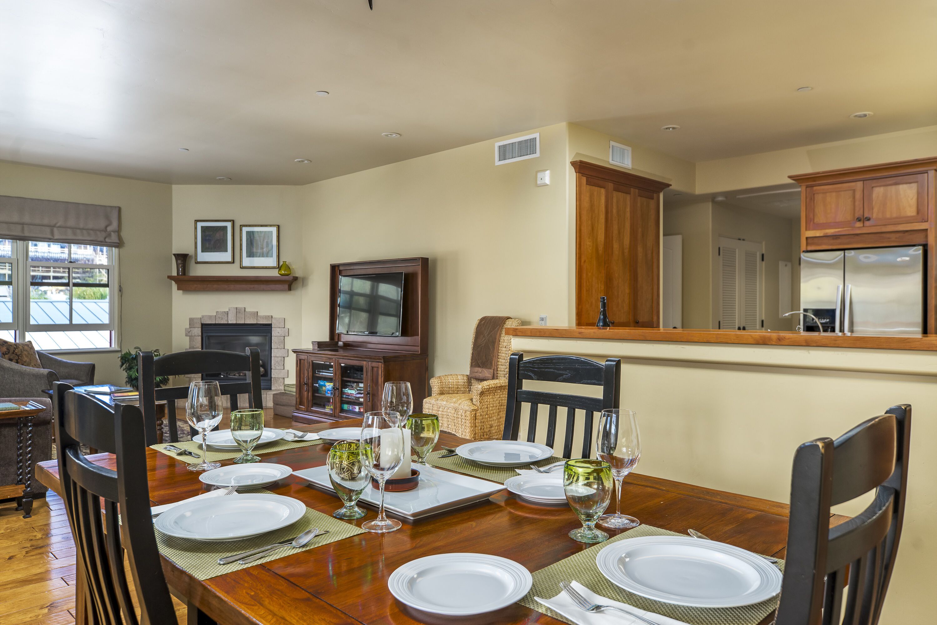 Une salle à manger avec une table en bois dressée pour six personnes, entourée de chaises, agrémentée d’une cheminée et d’un téléviseur.
