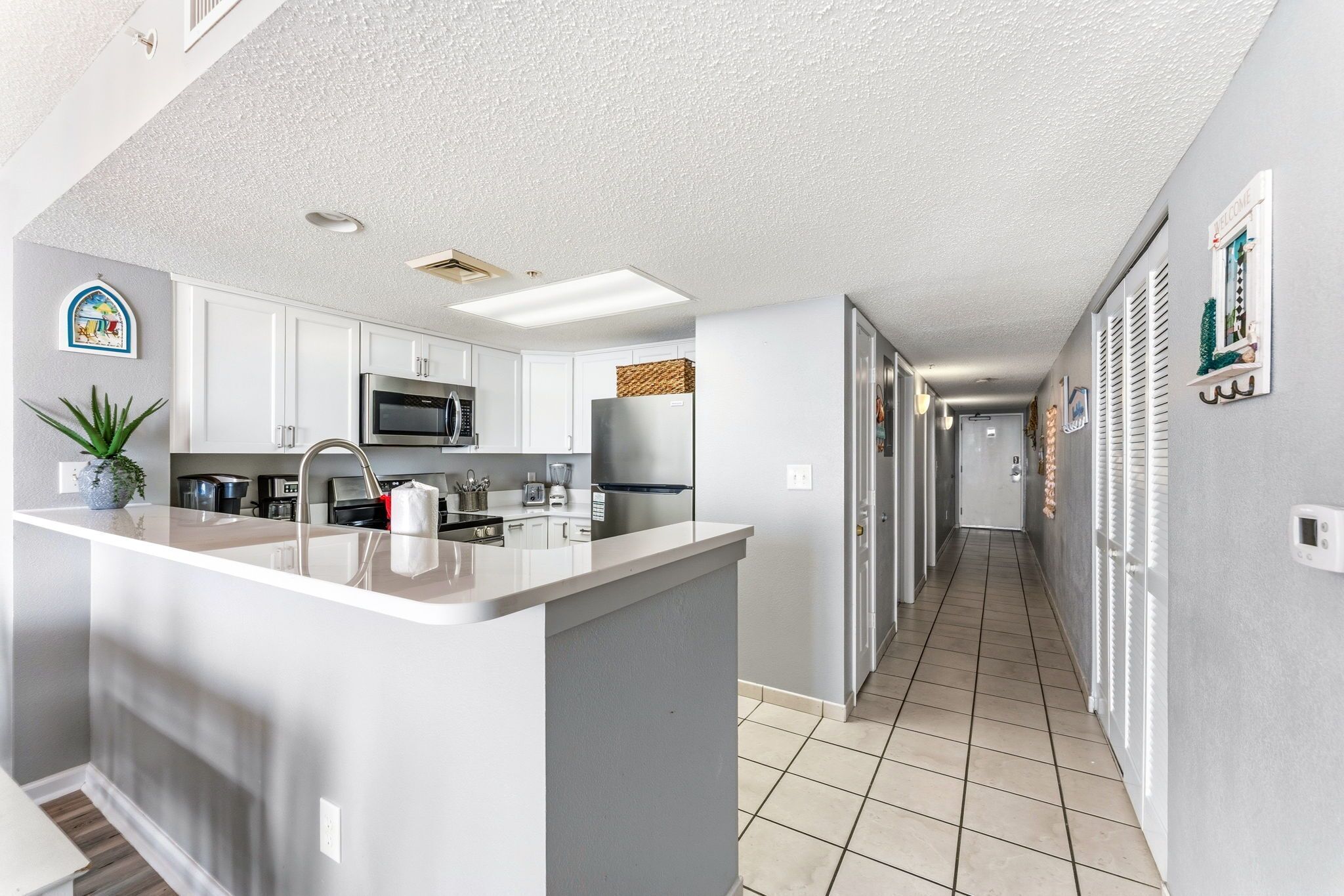 A modern kitchen with white cabinets, a central island, and a long hallway with a door at the end.