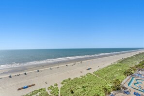 A beach view with a swimming pool, beach umbrellas, and a lifeguard tower. - Recently Renovated Oceanfront condo at great resort +Free Attraction Tickets! (North Myrtle Beach)