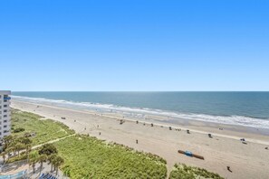 A beach with a clear view of the ocean, a sandy shore, and a building in the background.