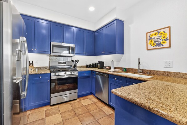 A kitchen with blue cabinets, stainless steel appliances, granite countertops, and a backsplash.