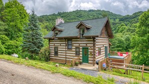 Une cabane en rondins avec une porte verte, une terrasse avec des chaises rouges et un paysage forestier pittoresque en arrière-plan.