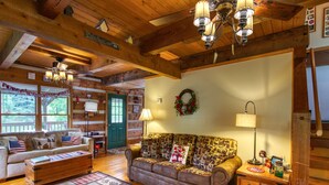 L’intérieur d’un chalet accueillant, avec un plancher en bois, un canapé agrémenté de coussins à motifs, une commode en bois et une porte verte.