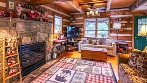L’intérieur d’un chalet avec une cheminée en pierre, un téléviseur, un canapé et une pancarte sur laquelle on peut lire : « Chalet, doux chalet ».
