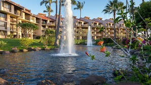 A hotel with multiple balconies, a central water feature with fountains, and surrounding greenery.