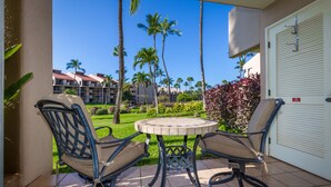 A patio with two chairs and a table, overlooking a well-maintained lawn and palm trees, with a building in the background.
