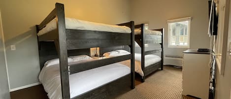 A room with two bunk beds, a ceiling fan, a window, and a refrigerator.