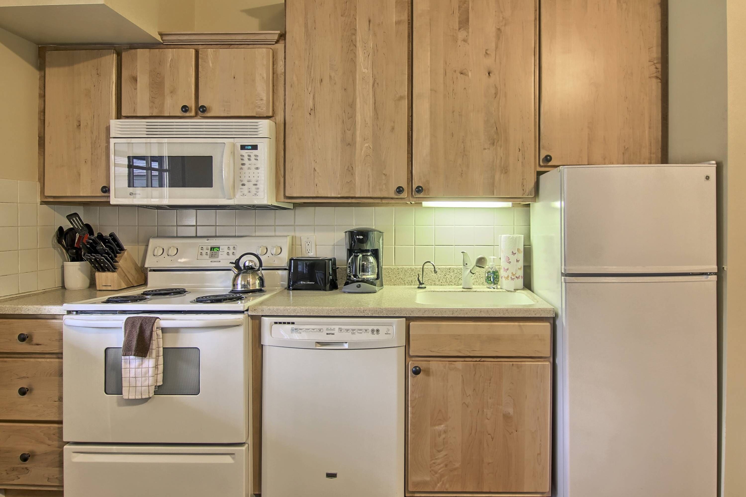 A kitchen with wooden cabinets, a microwave, a stove, a dishwasher, and a refrigerator.