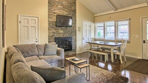 A living room with a stone wall, a fireplace, a television, and a dining area with a table and chairs. - Newly Renovated 4BR / 4BA Pet-Friendly, Best Walking Location At Boyne Mountain (Boyne Falls)