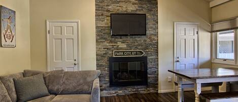 A living room with a stone fireplace, a television mounted above it, a couch, and a dining table.