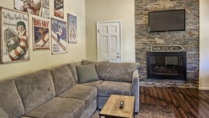 A living room with a sectional sofa, a fireplace, and vintage travel posters on the wall. - Newly Renovated 4BR / 4BA Pet-Friendly, Best Walking Location At Boyne Mountain (Boyne Falls)