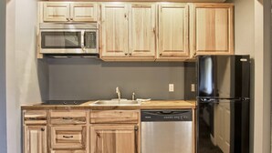 A kitchen with wooden cabinets, a stainless steel microwave, a dishwasher, and a black refrigerator. - Newly Renovated 4BR / 4BA Pet-Friendly, Best Walking Location At Boyne Mountain (Boyne Falls)