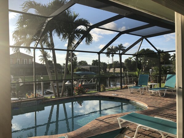 A pool area with a clear view of the surrounding landscape, including palm trees and a house.