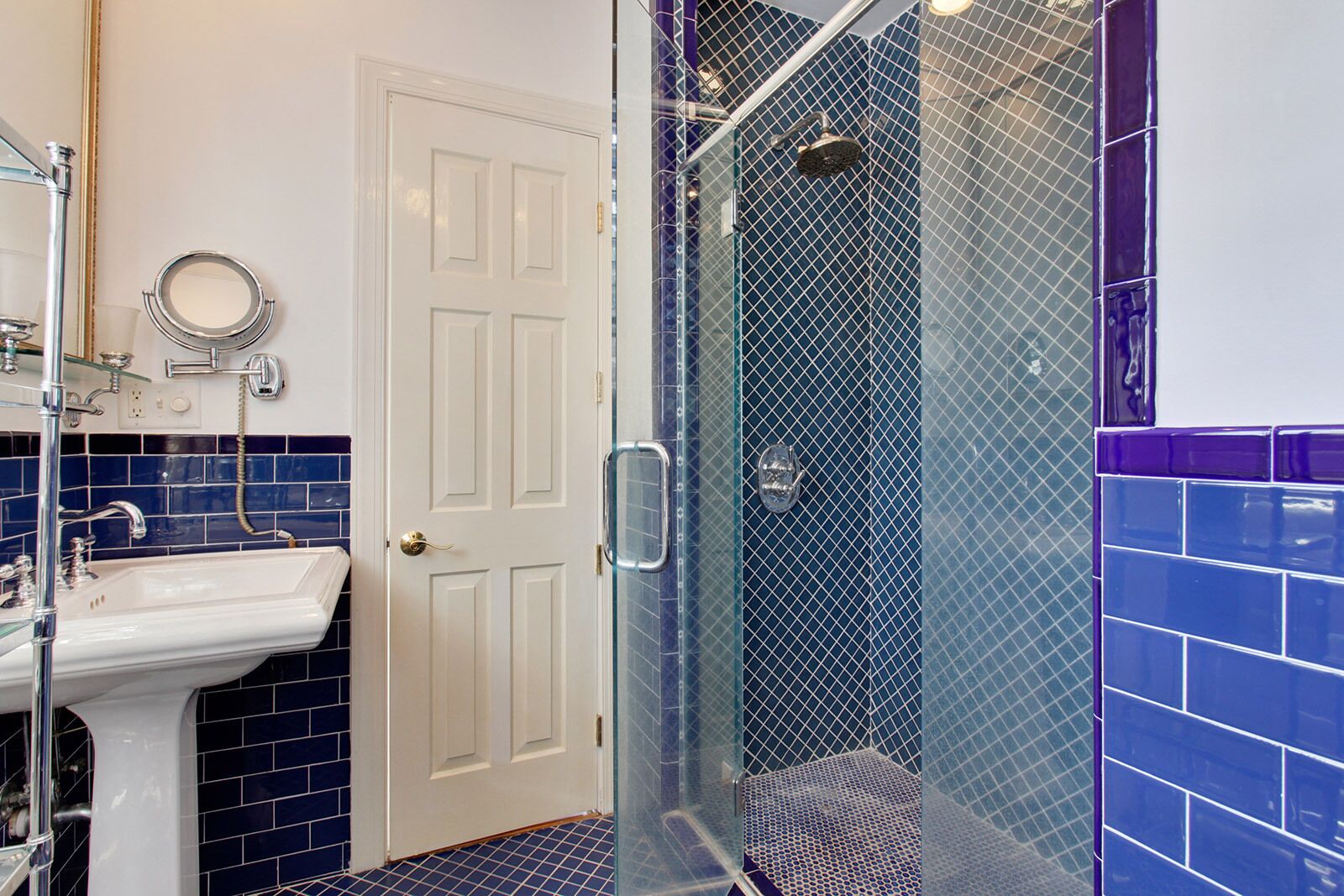 A bathroom with a white sink, a glass-enclosed shower, and blue-tiled walls.