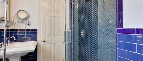 A bathroom with a white sink, a glass-enclosed shower, and blue-tiled walls.